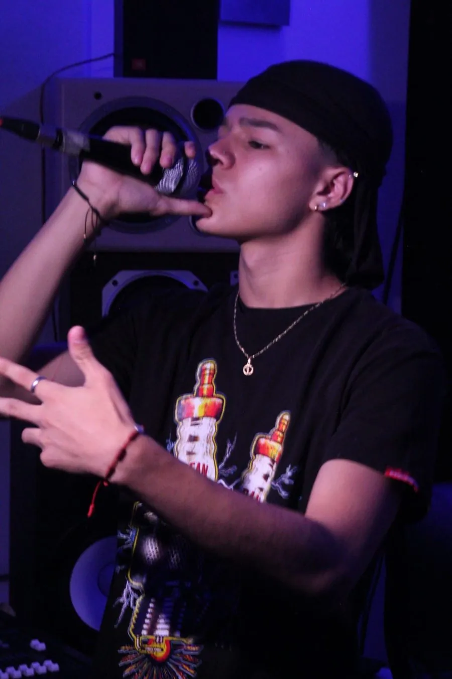 Mainyy cantando al micrófono, perfil, luz azul de estudio